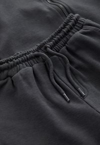 Pantalon de survêtement noir avec une taille élastique et des cordons de serrage, tissu doux au toucher, et une poche latérale zippée.