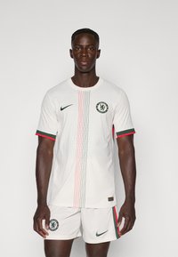 Maglietta da calcio Nike bianca con accenti verdi e rossi, caratterizzata da un motivo testurizzato, colletto rotondo e logo del Chelsea FC. Abbinata a pantaloni corti coordinati.