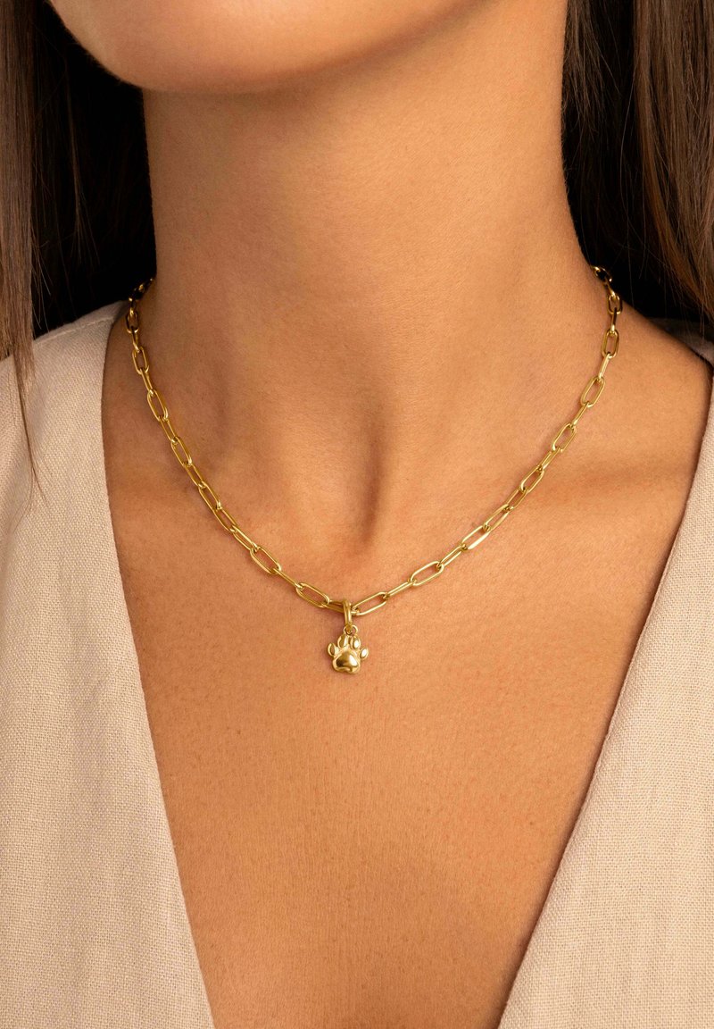 Collana in oro con maglie allungate e un ciondolo a forma di zampa, appoggiata su uno sfondo di tessuto neutro.