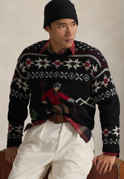 Μαύρο πλεκτό πουλόβερ με κόκκινες και λευκές διακοσμήσεις που απεικονίζουν έναν άνδρα με κόκκινα ρούχα. Φορεμένο πάνω από ένα κόκκινο και μαύρο καρό πουκάμισο, συνδυασμένο με μπεζ παντελόνι από κορδόνι.