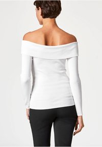 Haut blanc à manches longues avec épaules dénudées, en tissu côtelé, doté d'un large décolleté et d'une silhouette ajustée. Associé à un bas noir.