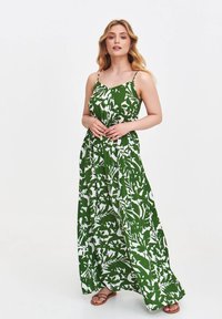 Grünes Maxikleid mit weißem Blattmuster, Spaghetti-Trägern und einer fließenden Silhouette. Der Stoff erscheint leicht und hat eine glatte Textur.