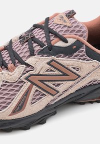 Zapatilla New Balance con parte superior de malla y ante en rosa y beige con acentos negros, logo destacado y suela texturizada.