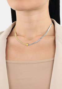 Collana in oro e argento con un design elegante e curvo; presenta un accento in oro levigato e una catena d'argento con sezioni testurizzate.