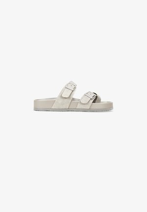 Sandalia deslizante de ante en tono beige con dos hebillas ajustables, suela plana y plantilla texturizada para mayor comodidad. Diseño simple y minimalista.