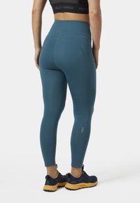 Hoge taille leggings in teal, gemaakt van rekbaar materiaal. Gladde textuur met zijzakken en een klein logo nabij de enkel.