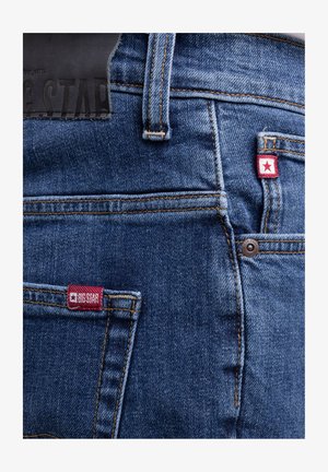 Denim-Jeans Rückentaschenbereich mit rotem BIG STAR Aufnäher, Gürtelschlaufe, Metallniete und detaillierter oranger Naht auf blauem Stoff.