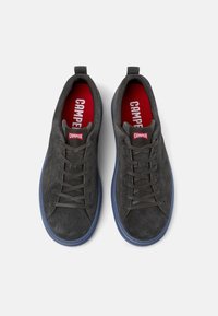 Grijze suède sneakers met een lage profiel, ronde neus en geperforeerde details. Voorzien van een rode binnenzijde en een blauwe rubberen loopzool.