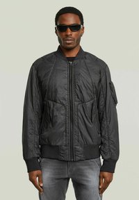 Giacca bomber nera realizzata in materiale leggero, con chiusura frontale con zip, polsini a costine e tasca laterale dalla texture liscia.