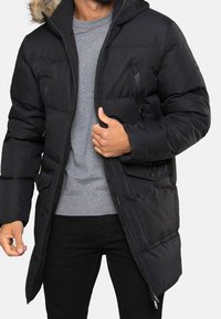 Schwarze Steppjacke mit einem Kapuzenfutter aus Pelz, ausgestattet mit einem Reißverschluss vorne, zwei Seitentaschen und einem eleganten, isolierten Design. Strukturiertes Gewebe.
