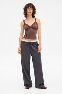 Brauner, mit Spitze verzierten Tanktop mit dünnen Trägern, kombiniert mit lockeren grauen Sweatpants, die einen elastischen Bund und einen Kordelzug haben.