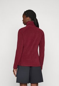 Bordeaux fleecejack met een hoge kraag, lange mouwen en een gladde textuur. Heeft zijnaden en een getailleerd ontwerp. Geen zichtbare logo's.