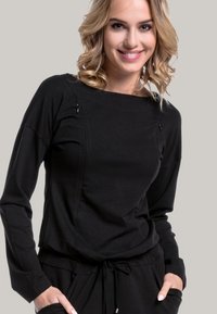 Black long-sleeve top in soft fabric with a boat neckline, featuring subtle stitching details and a relaxed fit. Paired with black pants.