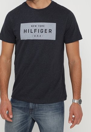 Tmavě šedé tričko vyrobené z bavlny, s modrým obdélníkovým logem s textem "NEW YORK HILFIGER U.S.A." Krátké rukávy a kulatý výstřih.