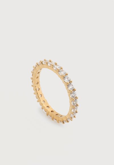 Bague à bande en or avec une rangée continue de pierres précieuses rondes et claires serties tout autour de la bande, sur un fond clair uni.