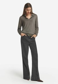 Langärmliges graues Poloshirt mit Kragen, kombiniert mit hochgeschnittenen, dunkelblauen Jeans mit Schlag. Spitz zulaufende braune Schuhe und ein strukturierter Gürtel sorgen für das gewisse Etwas.