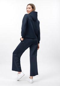 Sweat à capuche bleu marine avec une grande capuche, coupe décontractée et manches longues. Assorti à un pantalon large bleu marine et des baskets blanches.