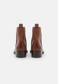 Hnědé kožené kotníkové boty s hladkým povrchem, elastickými bočními panely a nízkým blokovým podpatkem. Navrženy pro hladký, přiléhavý siluetu.