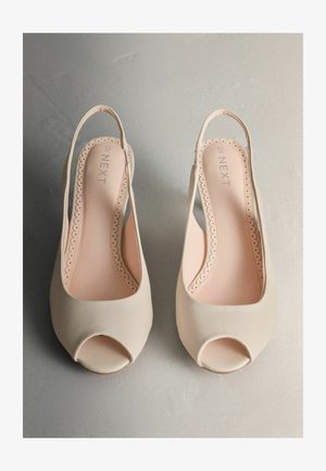 Beżowe sandały na obcasie z odkrytymi palcami, gładkim wykończeniem, falowanym obszyciem wokół wkładki i miękką wyściółką wewnętrzną.