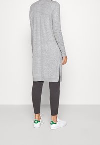 Harmaa pitkähihainen neulepaita, jossa sivuhalkiot, yhdistetty tummanharmaisiin joggereihin ja valkoisiin matalavartisiin tennareihin, joissa on vihreitä yksityiskohtia.