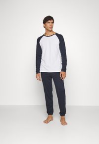 Mannenset voor loungewear met een witte langwerpige shirt met marineblauwe accenten en marineblauwe broek. Gemaakt van zachte, gladde stof, comfortabele pasvorm.