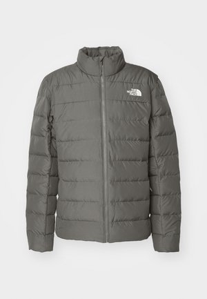 Gray puffer jacket with a high collar, horizontal quilted sections, front zipper, and a logo in the upper left corner.