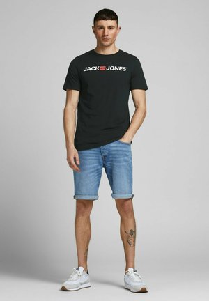 Schwarzes Baumwoll-T-Shirt mit weißem "JACK & JONES"-Logo, kombiniert mit hochgekrempelten Jeansshorts und weißen Sportschuhen. Flache, glatte Texturen.
