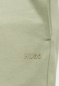 Φυστικί πλεκτό ύφασμα με κρυφό πλαϊνό τσέπη και ανάγλυφο λογότυπο "HUGO" σε ταιριαστό χρώμα κάτω από την τσέπη.