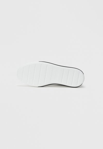 Sole of a black shoe with a white rubber bottom featuring horizontal grip lines on a plain light background.