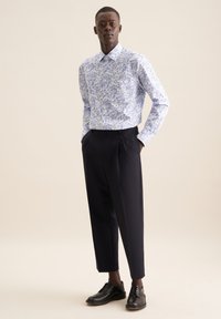 Camicia a maniche lunghe bianca con motivo floreale blu, abbinata a pantaloni neri su misura e scarpe nere stringate. Tessuto morbido, colletto con bottoni.
