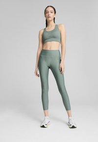 Minkštos žaliai sporto liemenėlė ir leggingų rinkinys, elegantiškas dizainas, pagamintas iš tamprios medžiagos, su subtiliu logotipo akcentu ir kontrastinėmis siūlėmis.