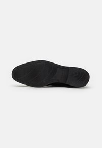 Suela de zapato negra con superficie texturizada y patrón hexagonal, con un borde liso y el logo "bugatti" grabado cerca del talón.