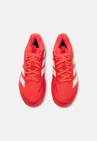 Red athletic shoes with a mesh upper, featuring white three-stripe accents, round toe, and textured rubber sole. Laces are matching red.