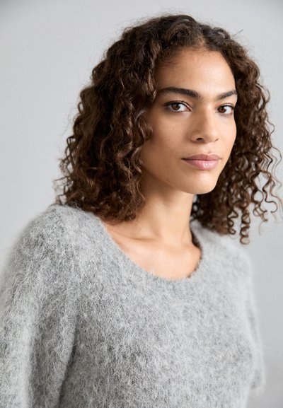 Γκρίζα φ fuzzy πουλόβερ με φαρδιά λαιμόκοψη και χαλαρή εφαρμογή. Η υφή των ινών είναι μαλακή και πλούσια, αναδεικνύοντας έναν ελαφρύ πλεκτό σχεδιασμό.