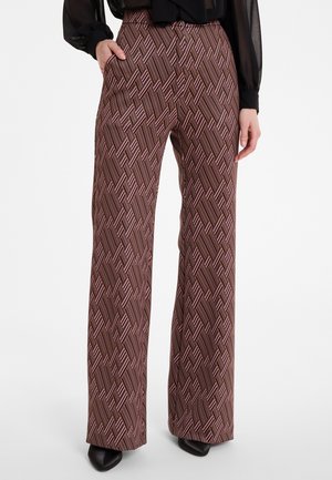 Woman wearing high-waisted wide-leg pants with brown and pink geometric pattern, black sheer blouse, and black pointed shoes.