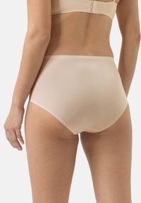 Mutande beige a vita alta realizzate in tessuto liscio, con un design uniforme e dettagli di cucitura minimi lungo l'elastico in vita e le aperture delle gambe.