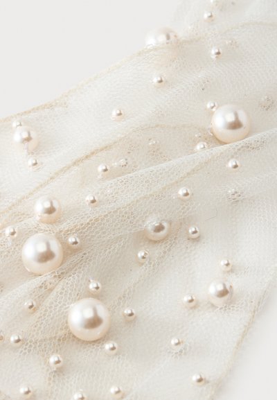 Tissu beige transparent décoré de perles petites et grandes dispersées de différentes tailles.