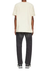 Crème kleur T-shirt met korte mouwen en een relaxte pasvorm, gecombineerd met donkergrijze tapered jeans. De outfit heeft zwarte sneakers met witte strepen.