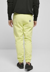 Pantaloni de trening de culoare verde lime, cu croi conic, manșete elastice și un buzunar la spate; purtați cu o cămașă neagră cu mânecă lungă și adidași negri.