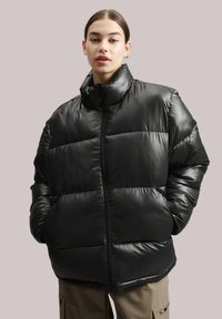 Melna pūkaina jaka ar augstu apkakli, gludu tekstūru un rāvējslēdzēja aizdari. Iespējas ietver kvadrātu formas siluetu un šūtas horizontālas zonas siltuma nodrošināšanai.