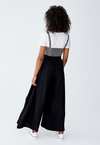 Zwarte culotte jumpsuit met een geruite bovenkant, elastische tailleband en wijde benen; gecombineerd met een wit t-shirt en witte sneakers.