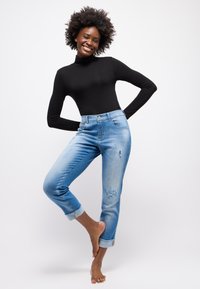 Helle blaue, ausgewaschene Jeans mit hoher Taille, umgeschlagenen Säumen und einem schwarzen, langärmeligen Rollkragenoberteil. Angenehmer Stoff und lässige Passform.