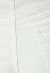 White denim fabric featuring slight texture, stitched seams, and a flap pocket detail, indicating a casual trouser design.