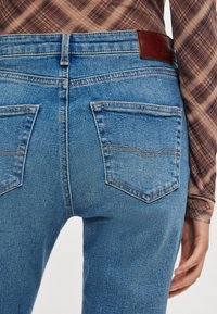 Jeans de mezclilla azul con cintura de altura media, diseño de cinco bolsillos y textura suave. Parche de cuero con la marca en la cintura trasera.