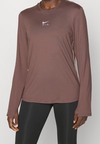 Brun långärmad träningsskjorta i mjukt tyg, med rund halsringning och en vit Nike AIR-logotyp på bröstet.