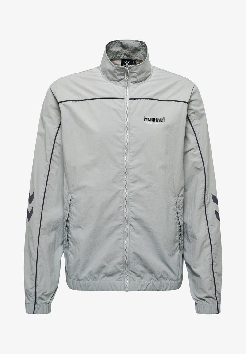 Chaqueta de cremallera gris claro hecha de tejido suave. Presenta líneas de acento negras y un pequeño logo en el pecho. Puños y dobladillo elásticos.