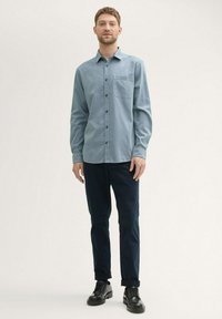 Camisa de botones de color azul claro, con mangas largas, bolsillo frontal y botones negros, combinada con pantalones azul marino y zapatos negros. Textura plana.