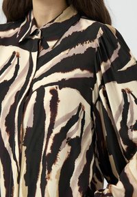 Langermet bluse i teksturert stoff med et beige, svart og brunt abstrakt dyremønster. Klassisk krage med knappelukking.