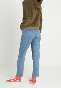 Fleecejacka med huood i olivgrön, ljusgrå nederkant, i kombination med blå högmidjade jeans och orangea Vans-sneakers.