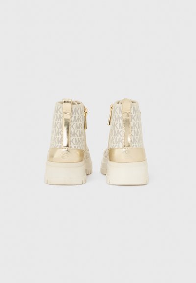Guldtonade ankellång stövlar med en texturerad off-white ovandel som har ett repetitivt logomönster. Dragkedja bak och ett handtag för enkel påtagning.